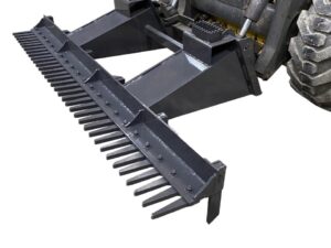 Close-up of a black metal landscape rake attachment, known as the Skid Steer Eliminator, connected to the front of a heavy-duty skid steer construction vehicle with large tires.