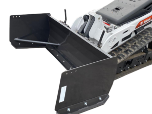 Close-up view of a Bobcat compact track loader featuring a large, black spreader attachment parked on an asphalt surface. Various other machinery and equipment, including a Mini Skid Steer Snow Pusher, are visible in the background.